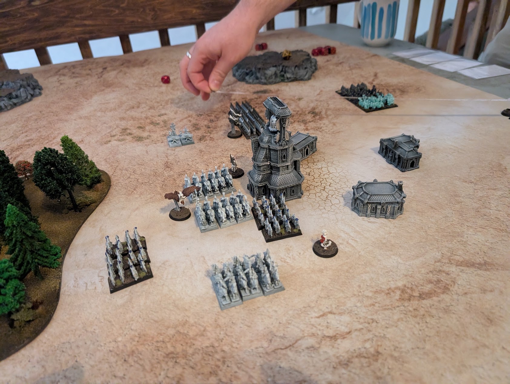 A player moves a Warmaster unit among ranks of troops surrounding a ruined tower near woodland.